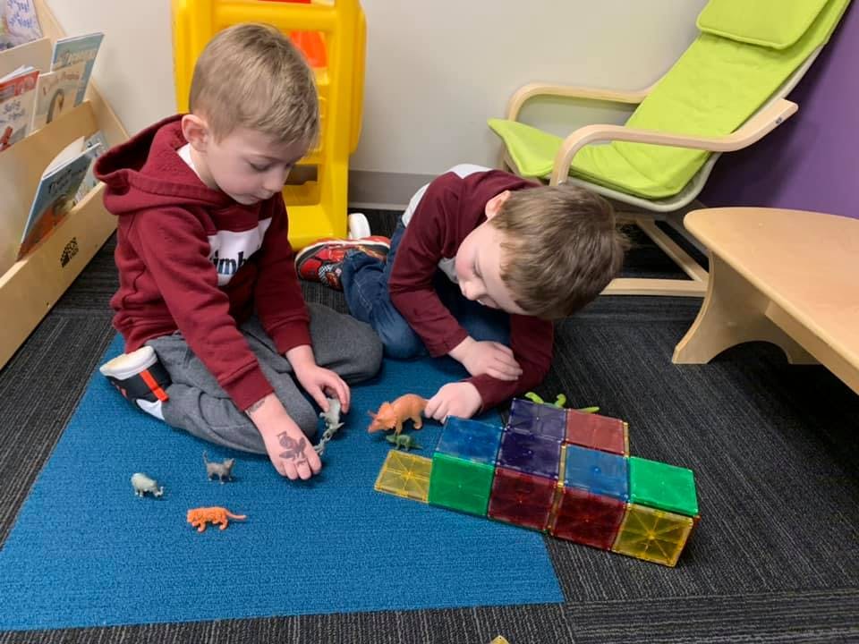 Two children playing with magnetic tiles and animal figurines on a blue mat