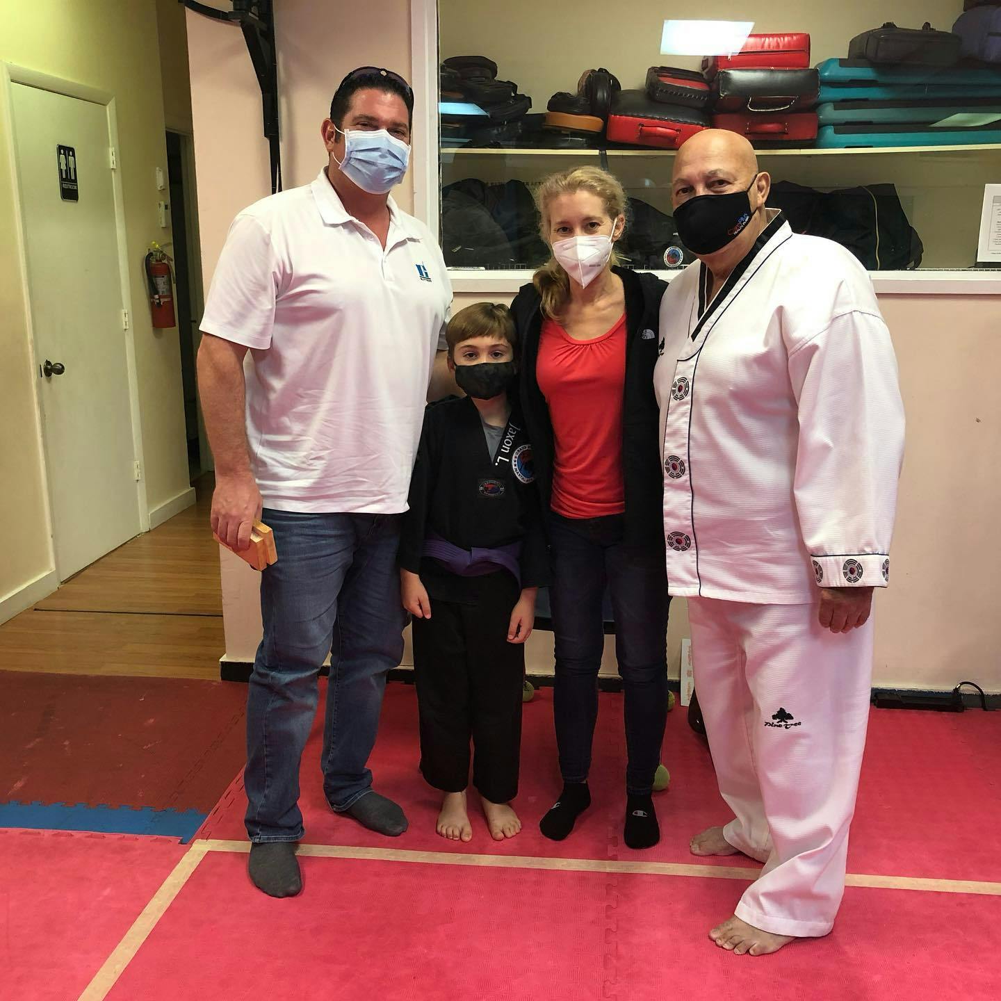 Four people wearing face masks standing on a red mat