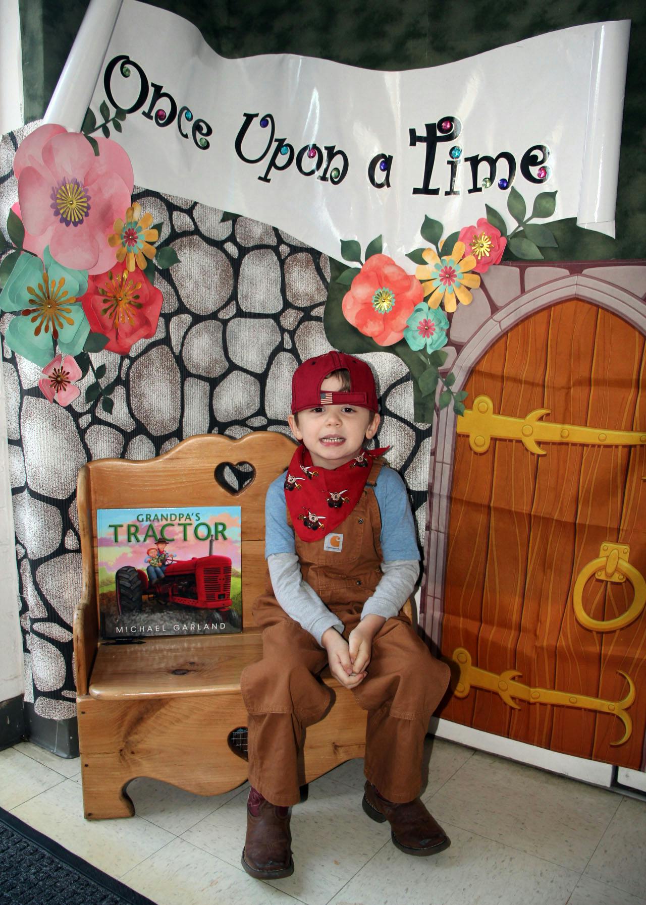 Child sitting on a wooden bench with a book, in front of a backdrop