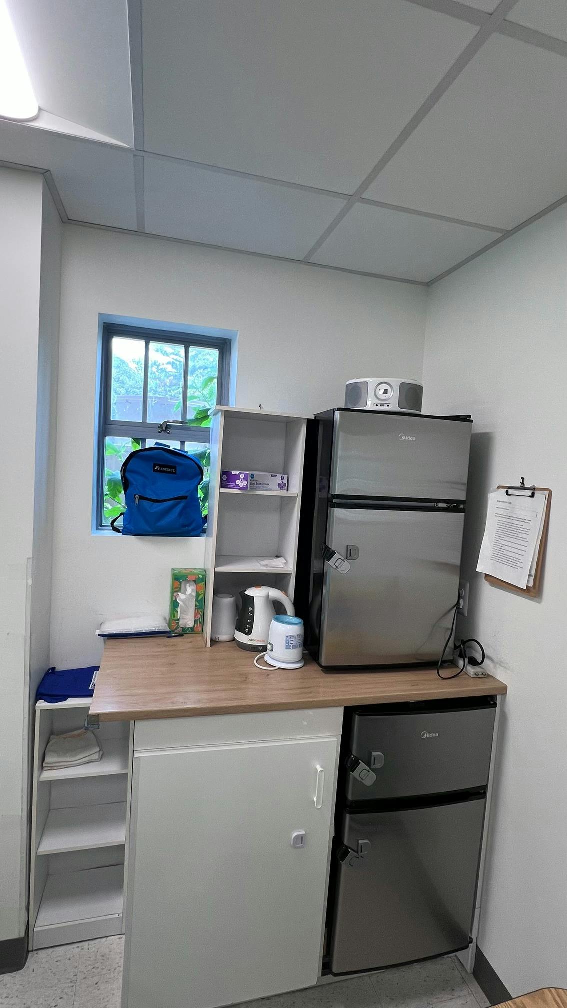 Small kitchen station with a mini fridge, shelving, and electric kettle