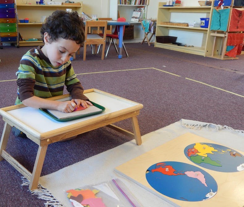 Child drawing on paper at a small table in a classroom