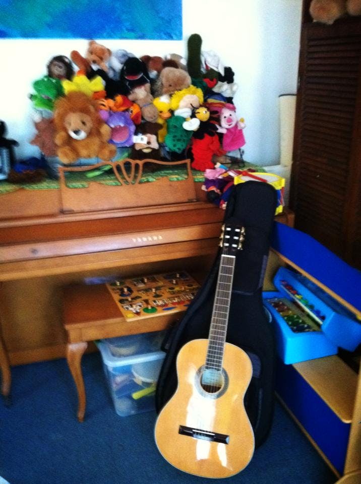 Guitar leaning against a piano with stuffed animals on top