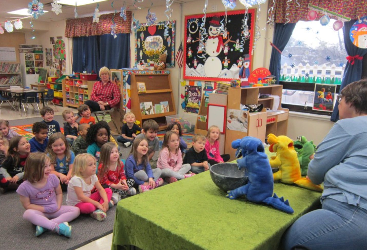 Children sitting on the floor watching a person with puppets in a classroom