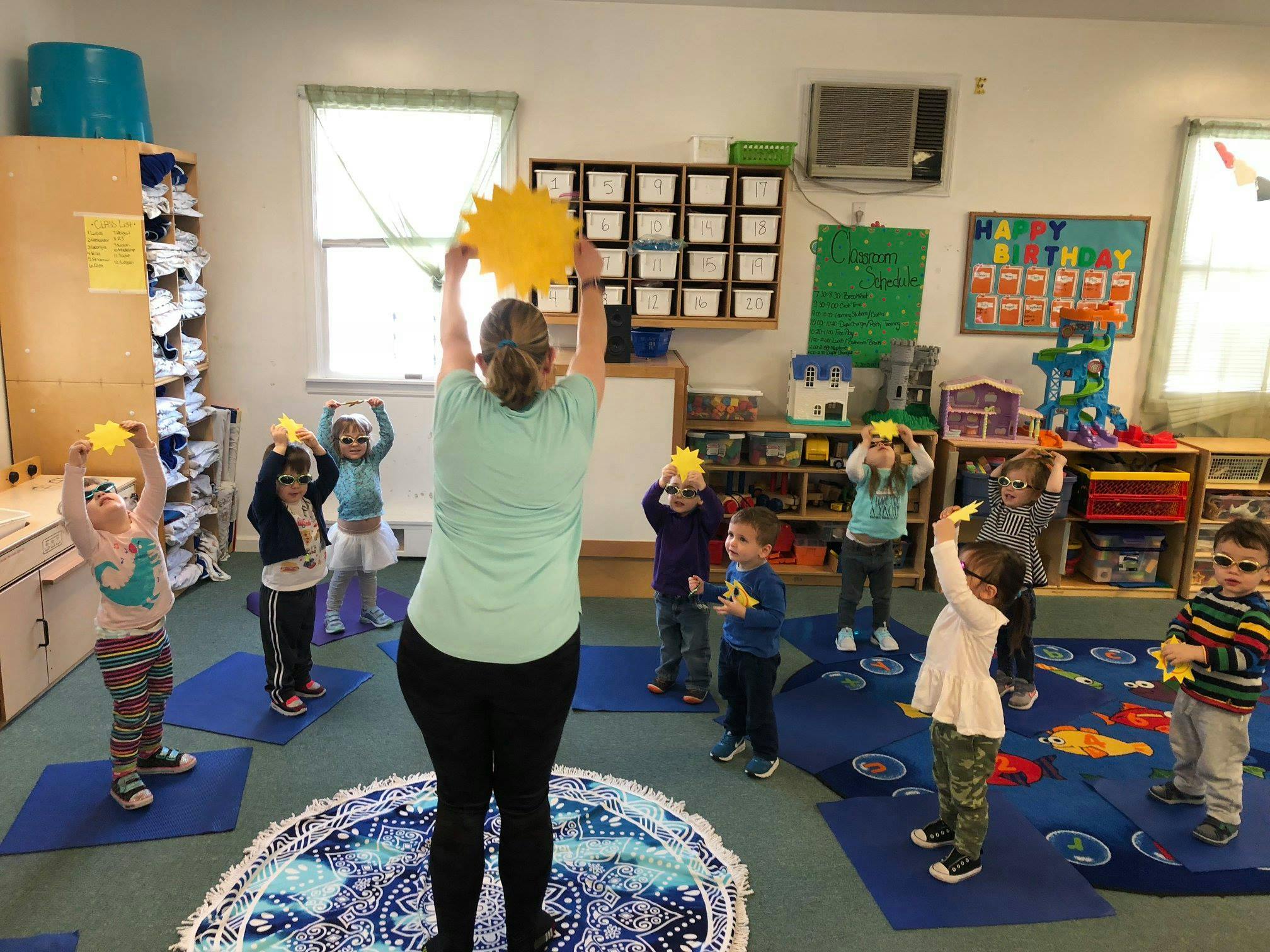 Adult and children holding up yellow sun cutouts in a classroom