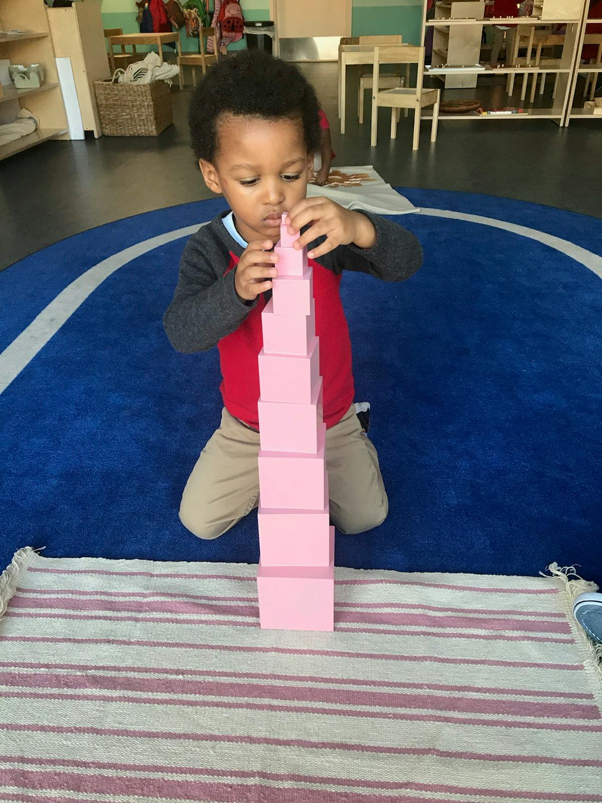 Child kneeling and stacking pink blocks