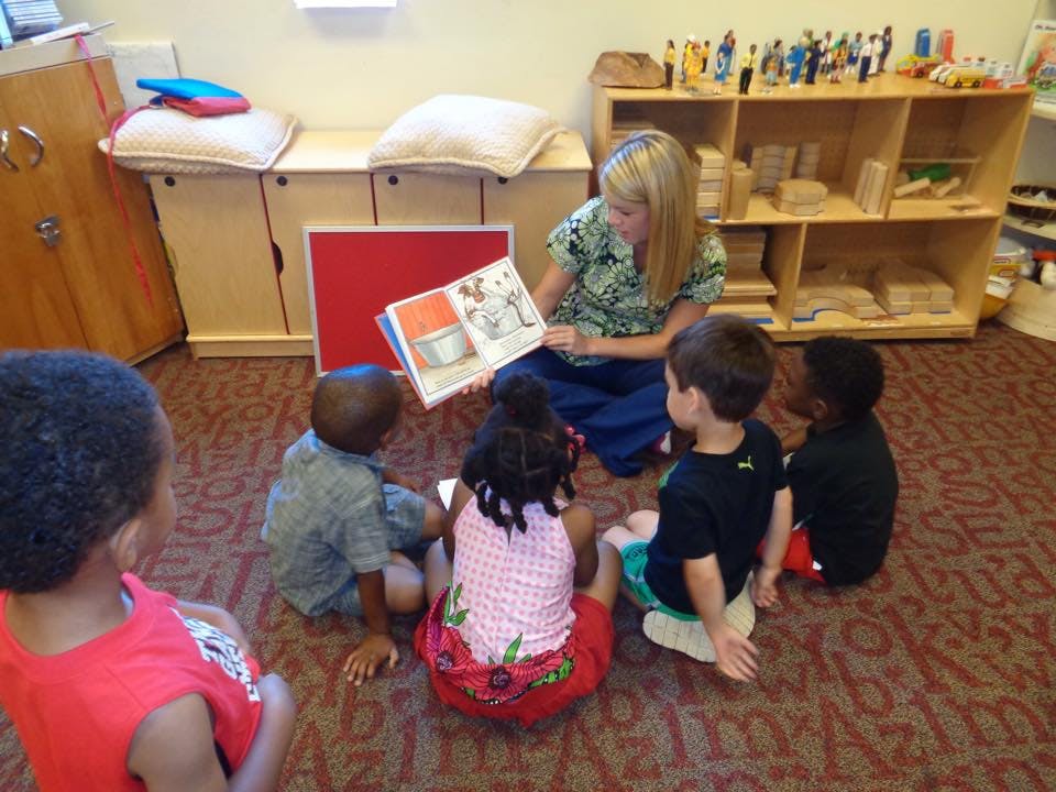 Person reading a book to four children in a classroom