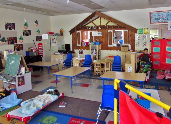 Child sleeping on a cot in a classroom with tables and chairs