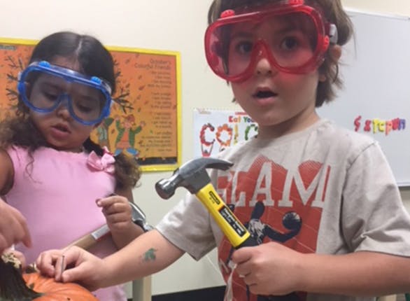 Two children wearing safety goggles, one holding a hammer