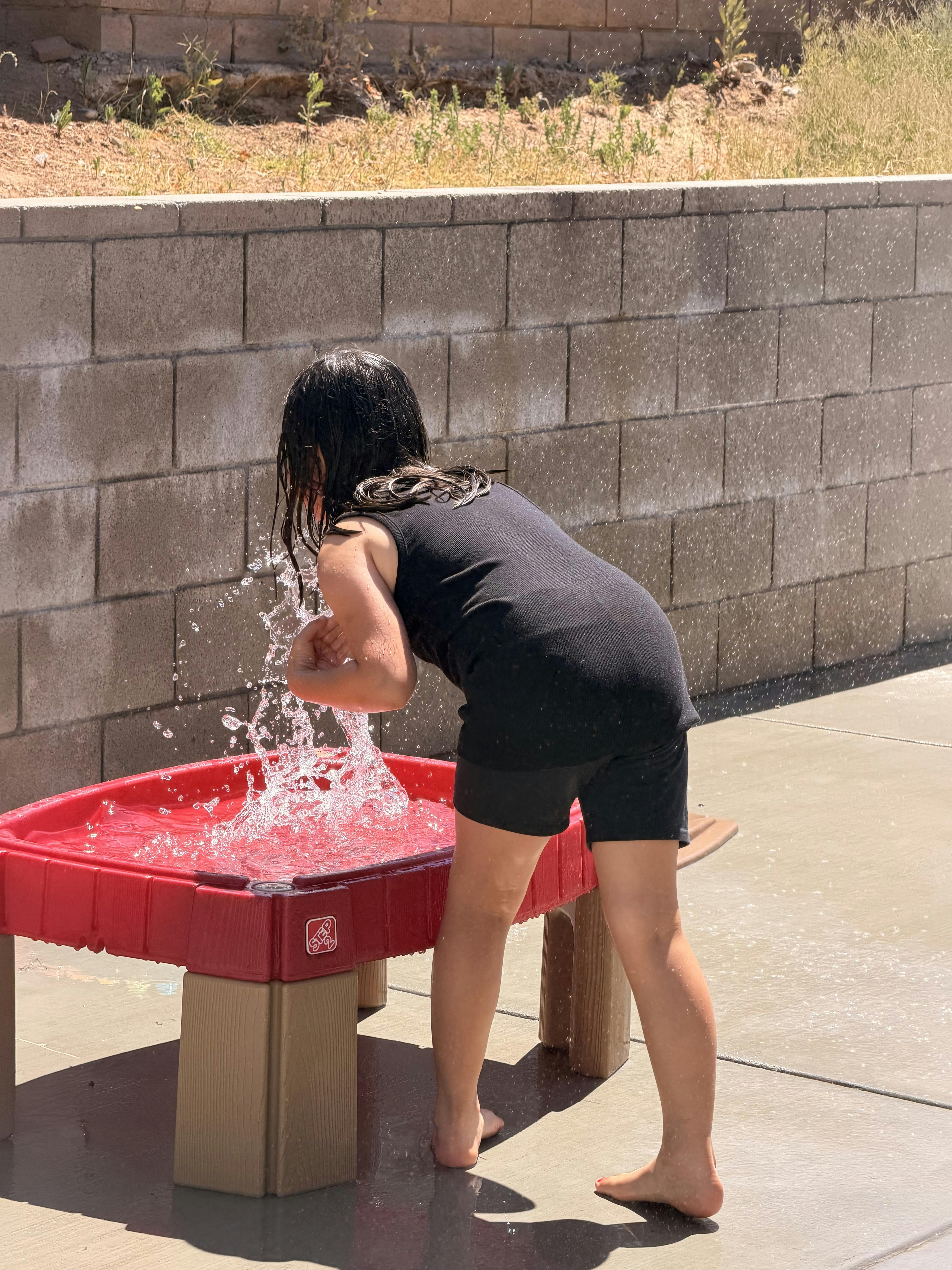 Child splashing water in a plastic outdoor table