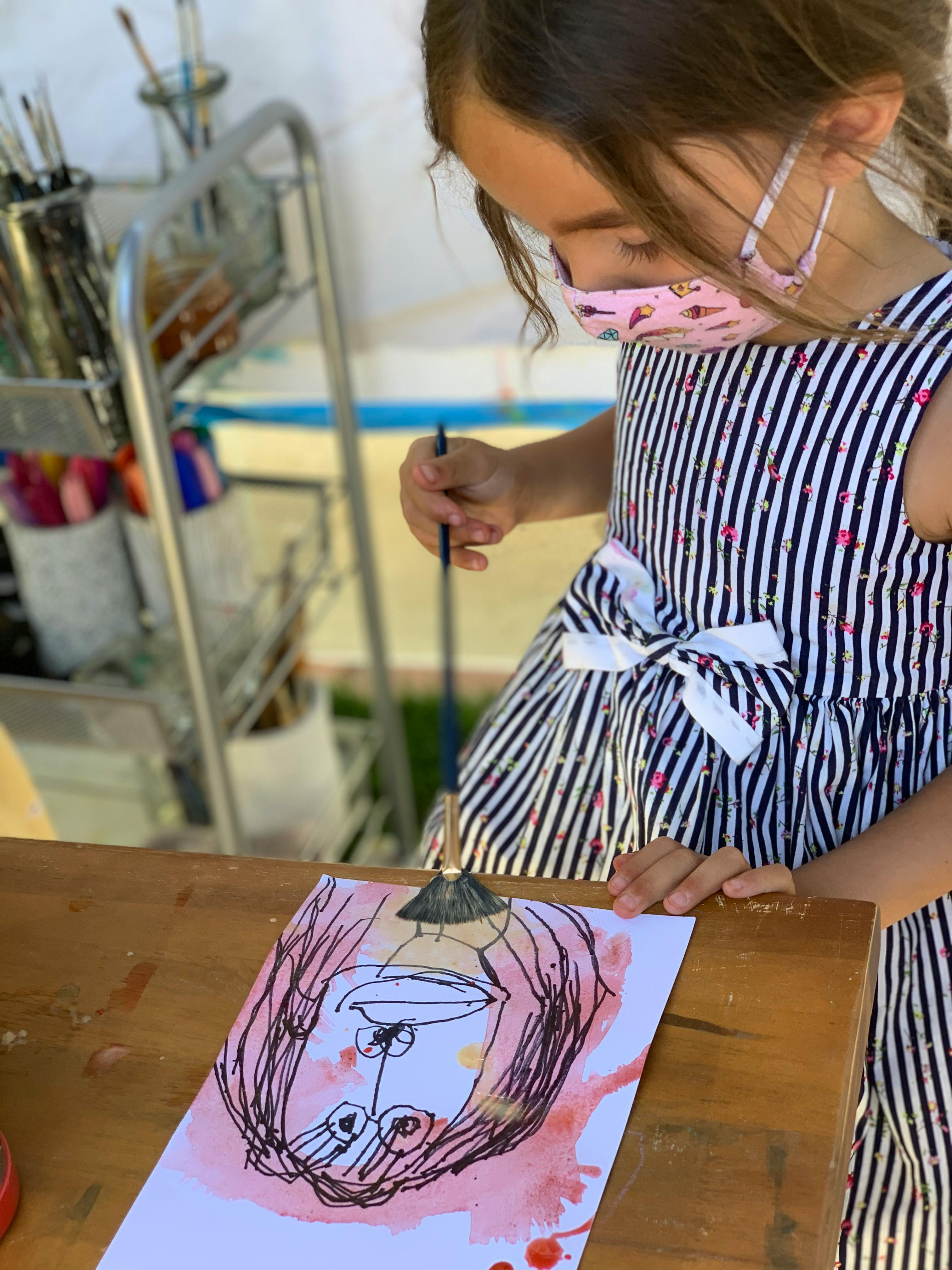 Child in a mask painting a picture of face on paper