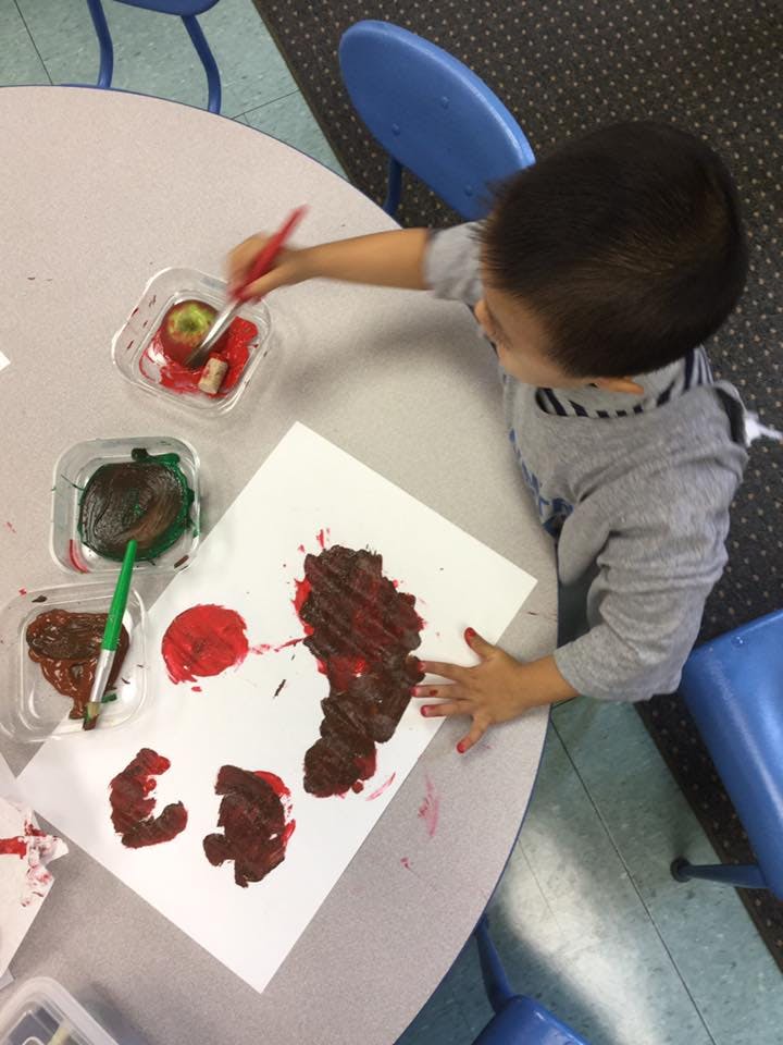 Child painting with a brush and apples on paper