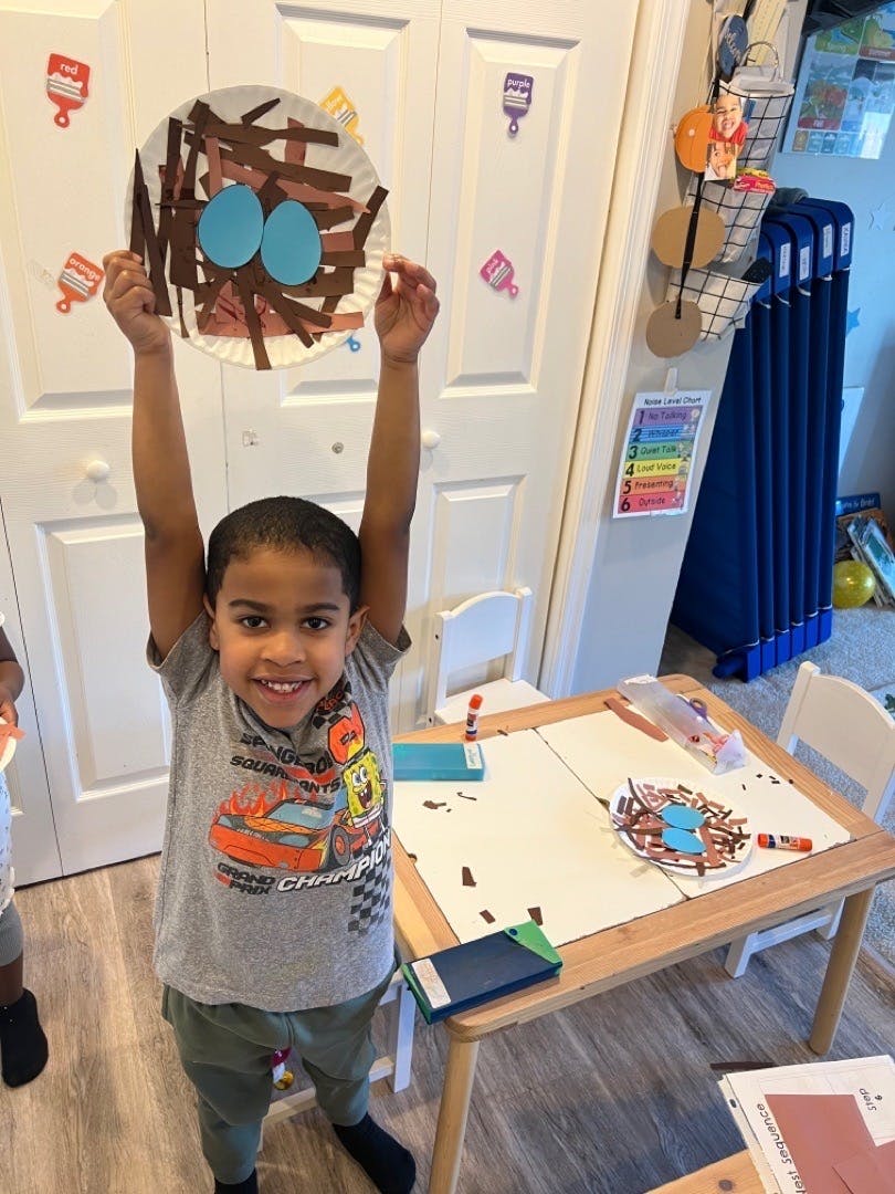 Child holding up a paper plate craft of a bird's nest with two blue eggs