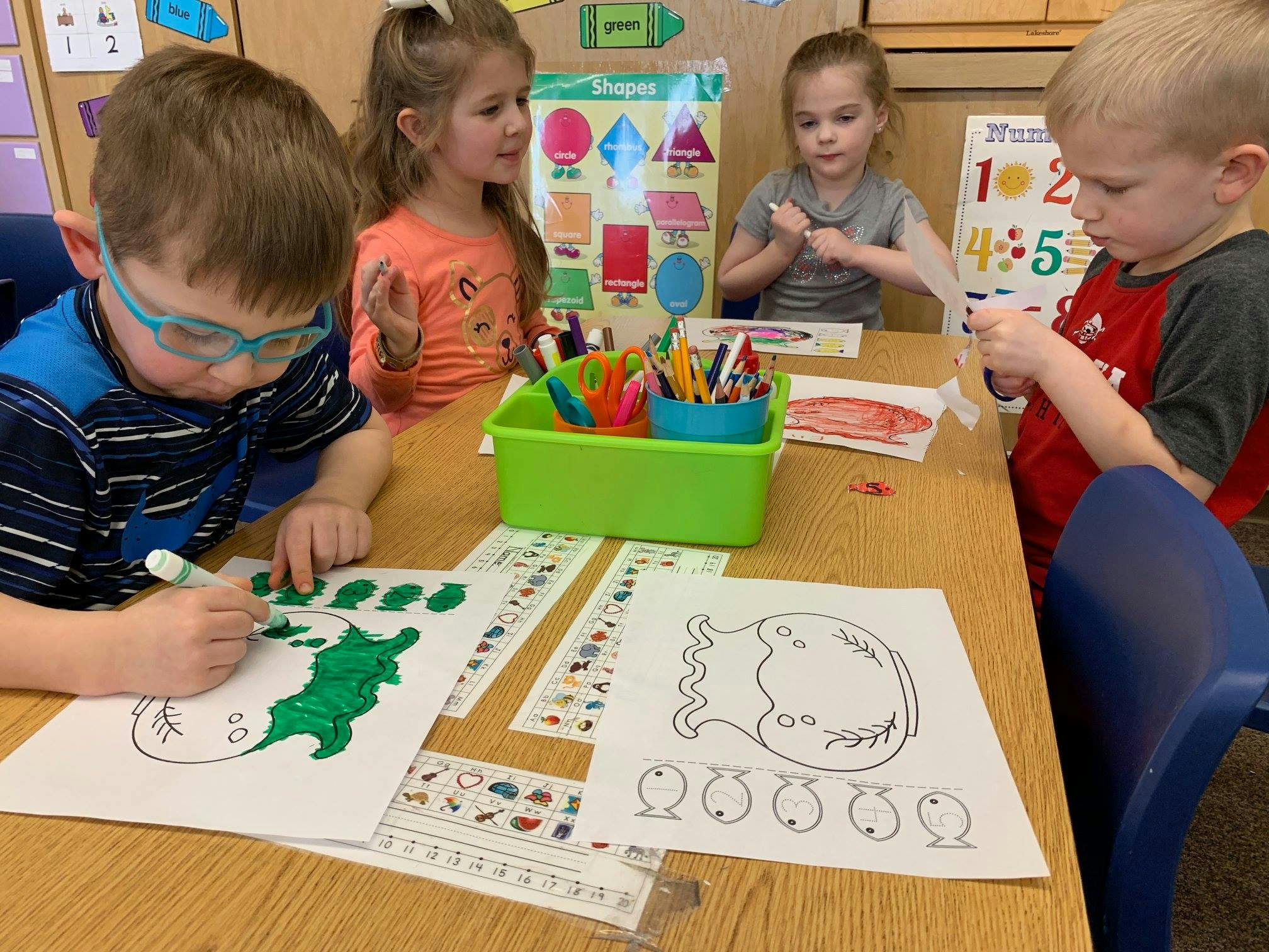 Four children coloring and crafting at a table in a classroom