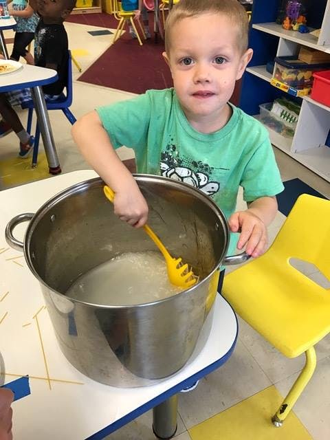 Child stirring a large pot with a yellow utensil