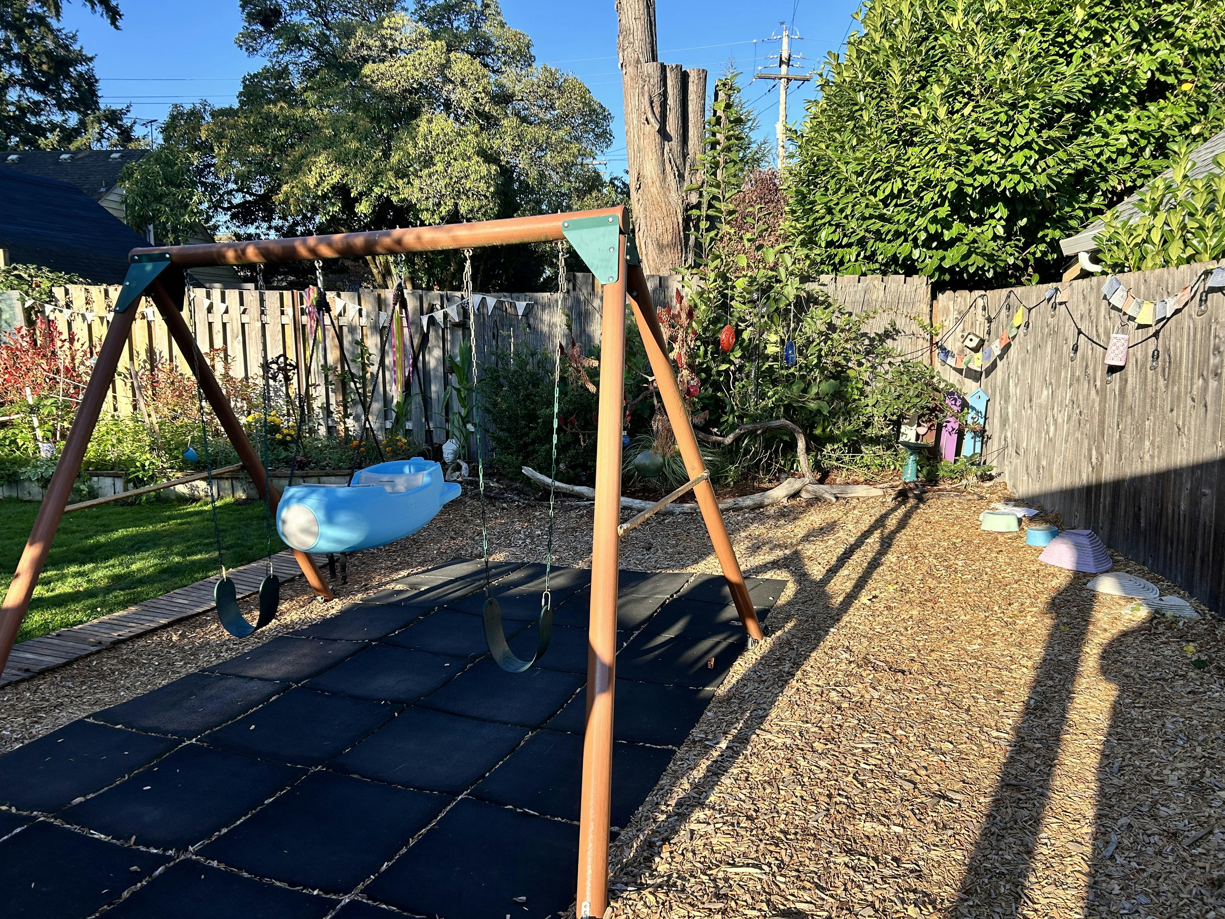 Backyard swing set with a blue glider and standard seats on rubber matting