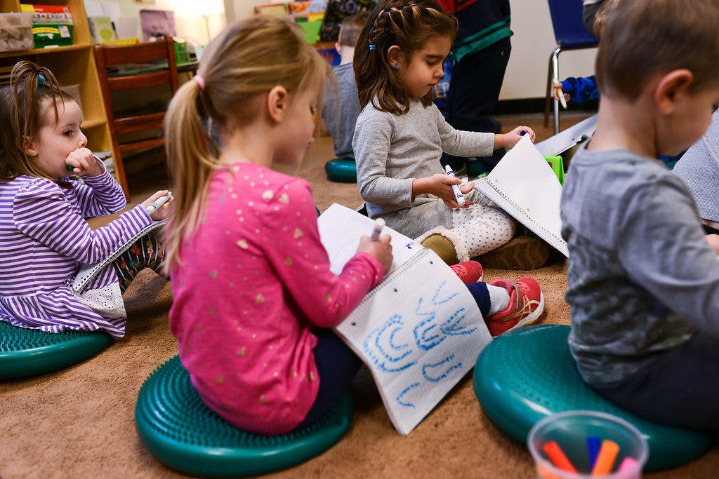 Children sitting on cushions and drawing in a classroom