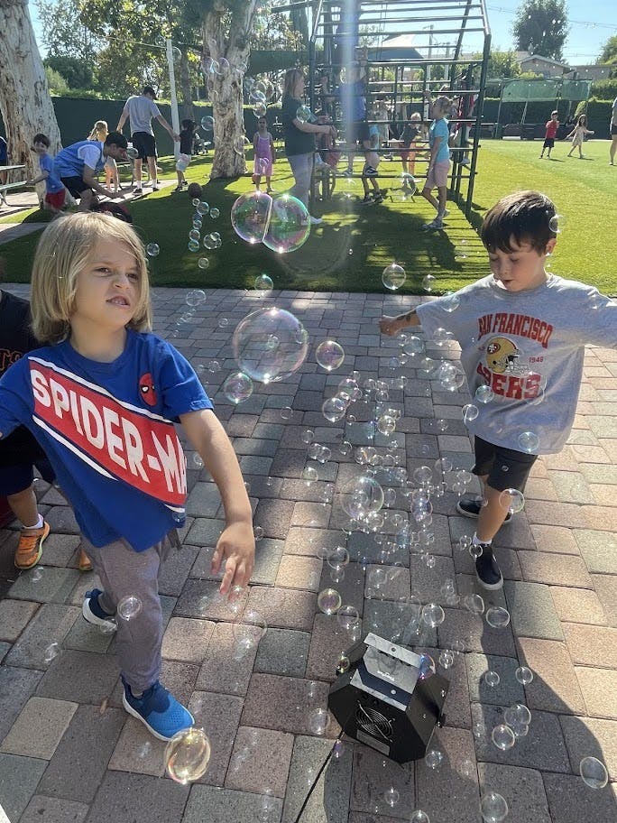 Two children playing near a bubble machine outdoors