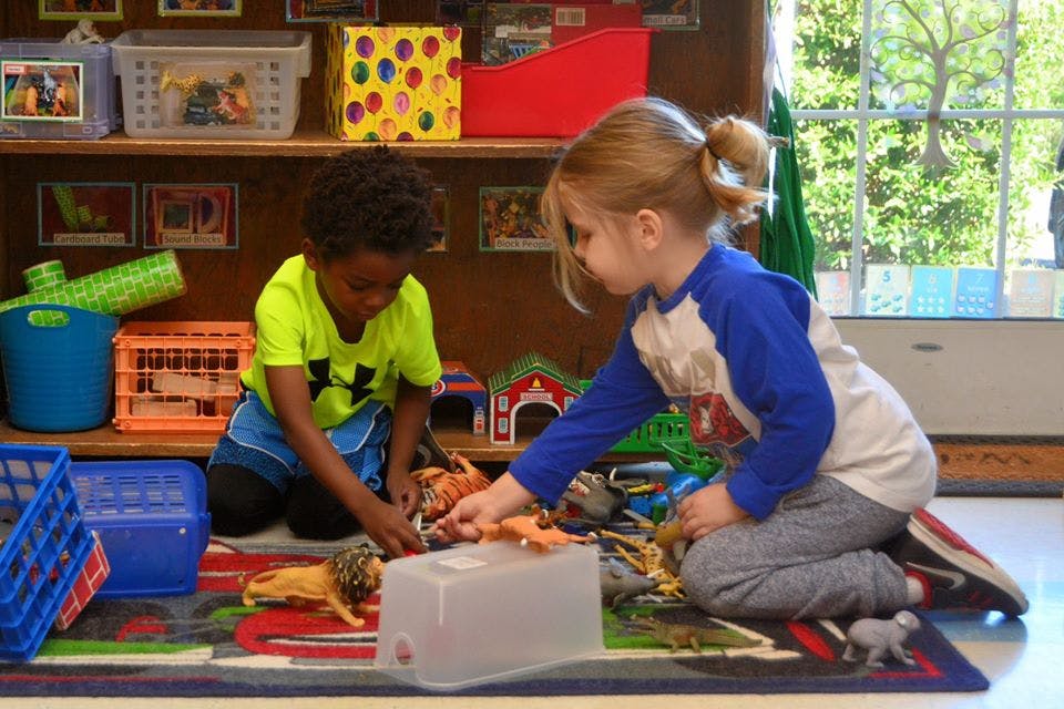 Two children playing with toys on a rug in a classroom