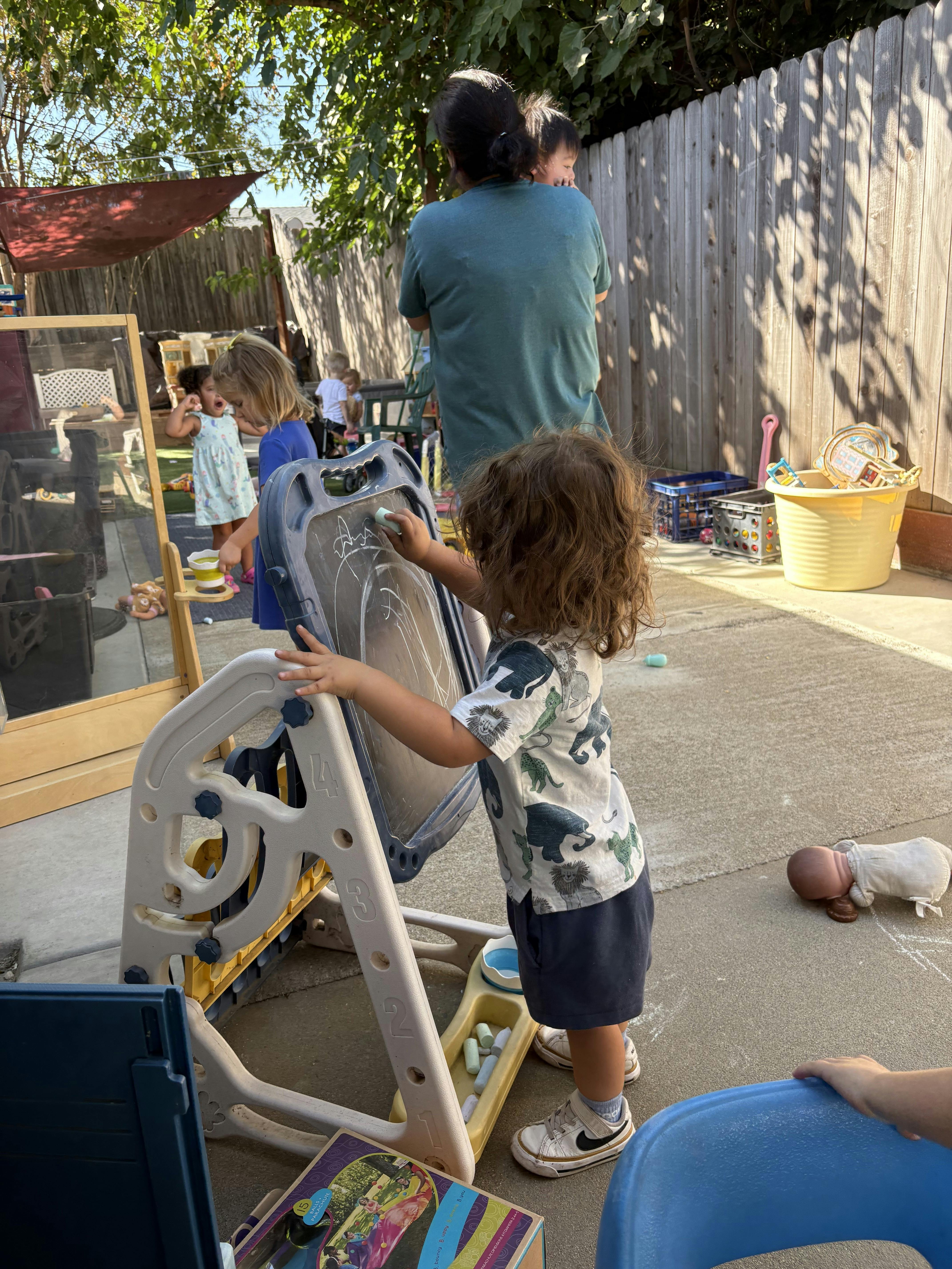 Child drawing with chalk on an easel in a backyard with other people