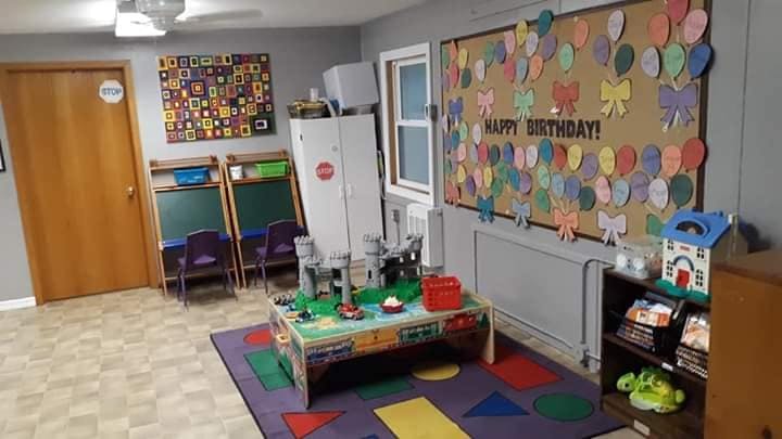 Playroom with a table, rug, easels, and a "Happy Birthday" bulletin board