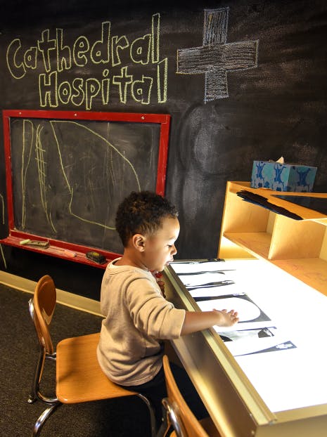Child sitting at a light table with papers, a chalkboard in the background