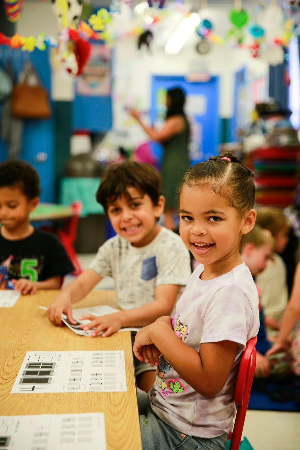 Three children sitting at a table with papers in a classroom