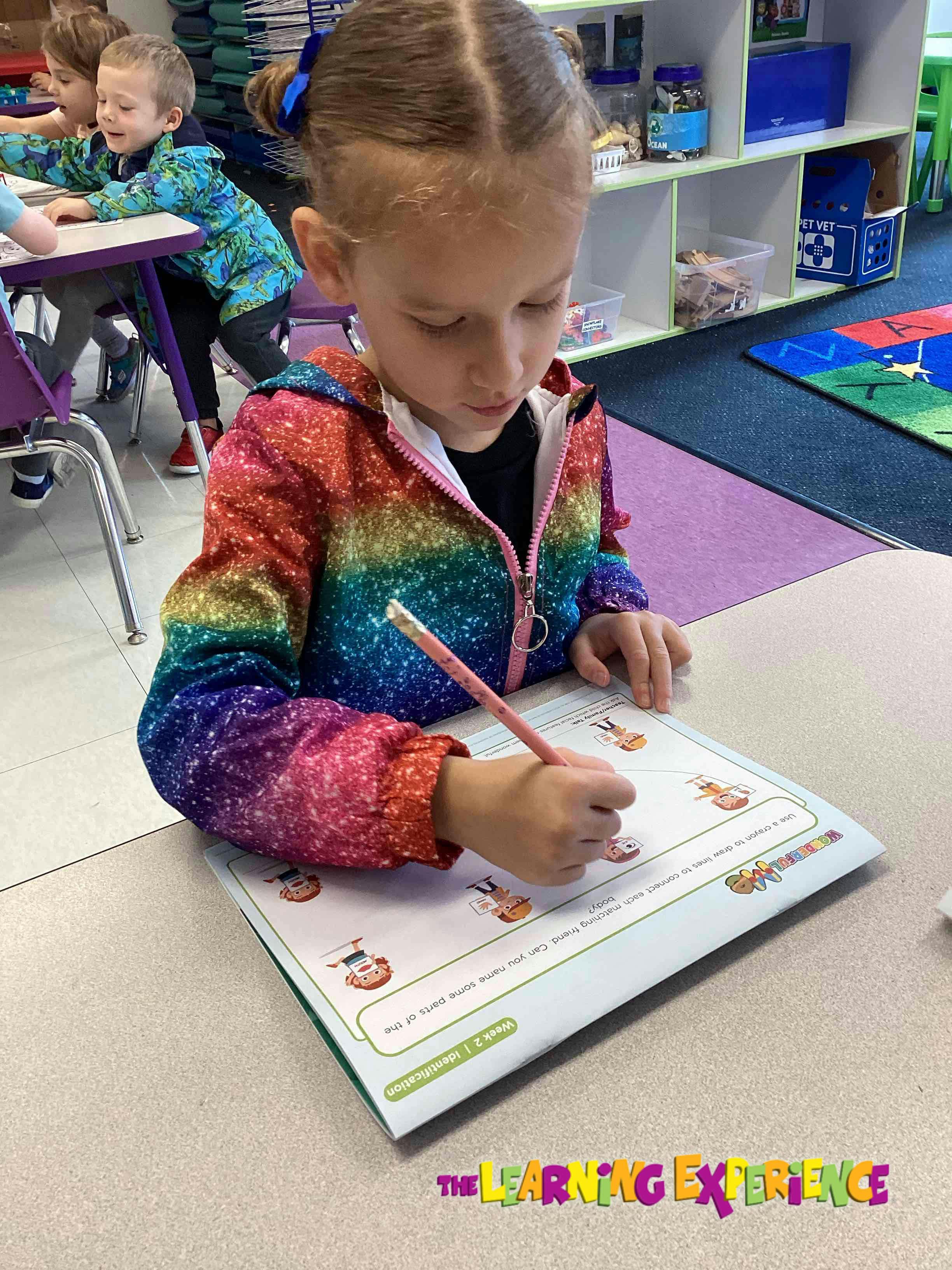 Child writing on a worksheet at a desk in a classroom