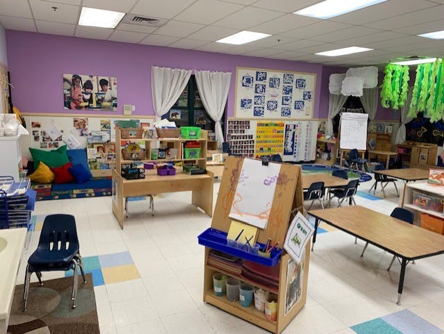 Empty classroom with tables, chairs, shelving, and art supplies