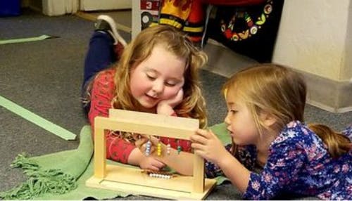 Two children lying on floor playing with a wooden abacus toy