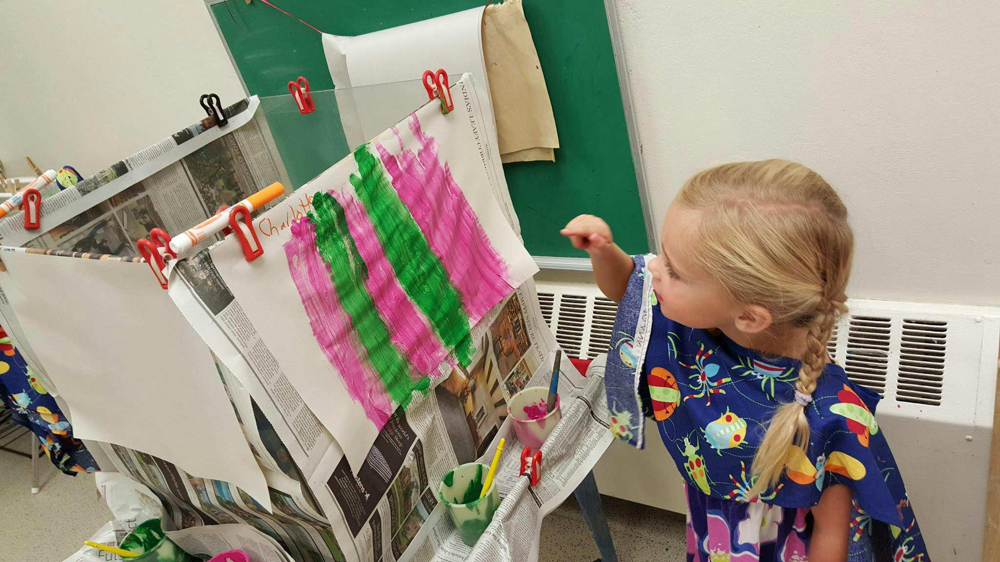 Child looking at colorful drawings hanging on a drying rack