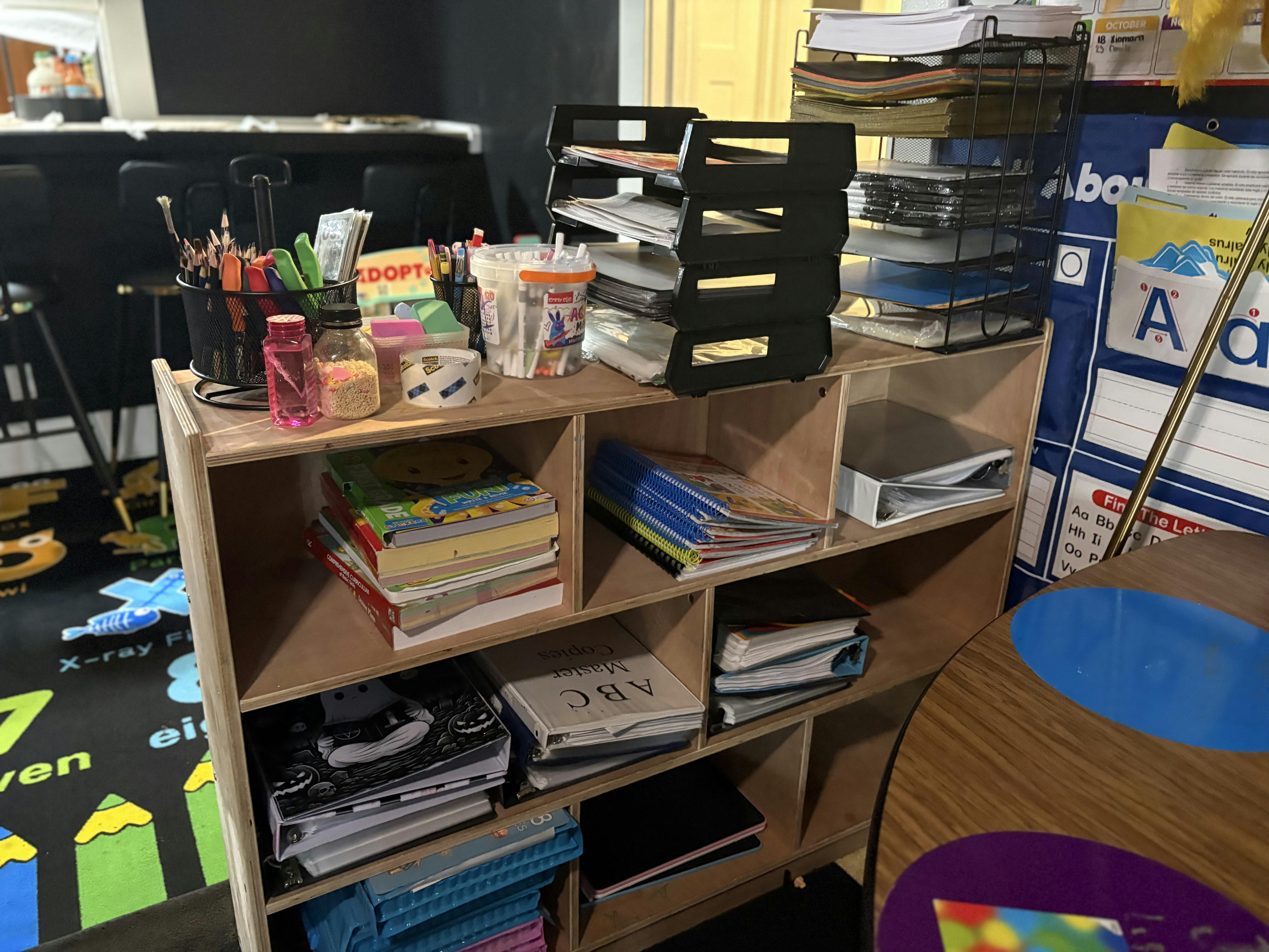 Wooden shelving unit filled with classroom supplies and stacks of books