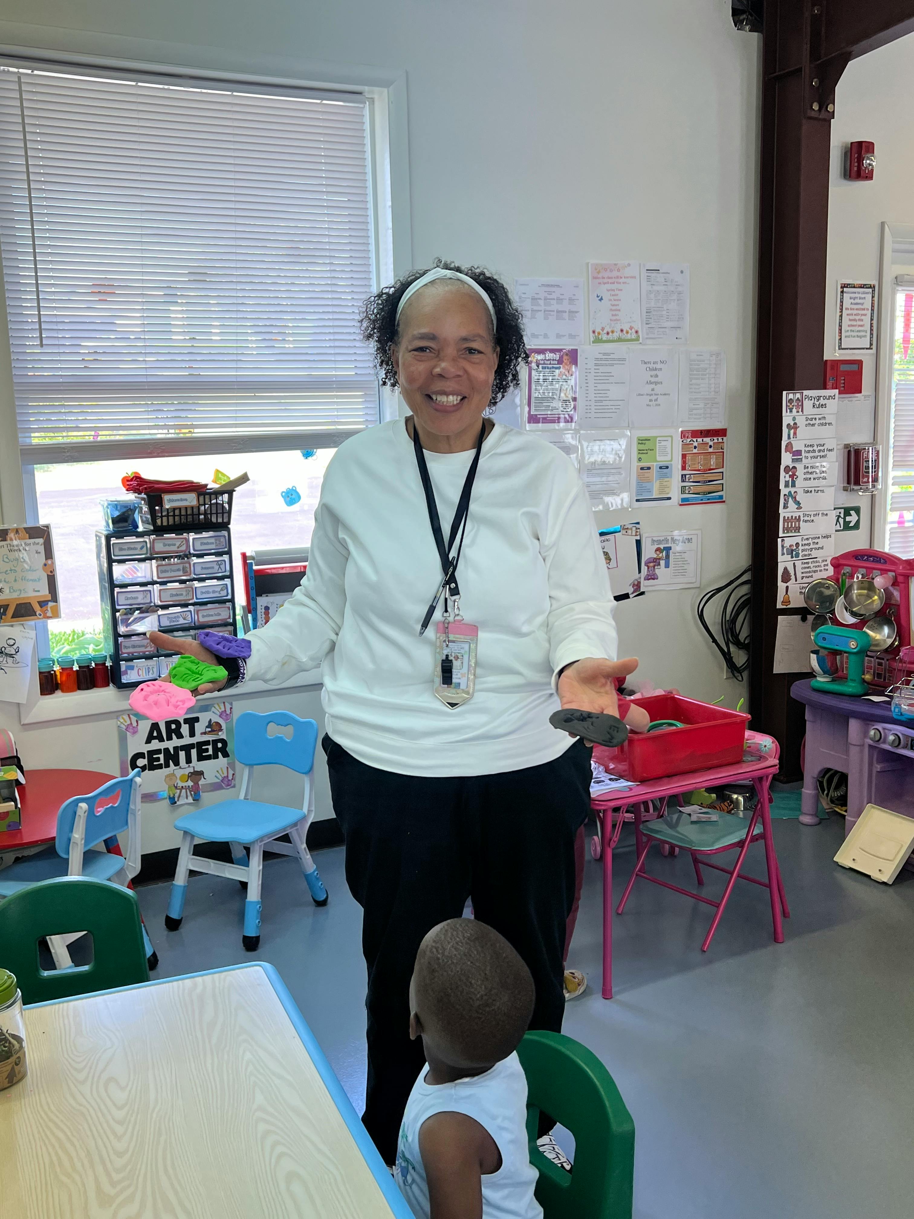 Smiling person standing with a child in a classroom, holding up a small object