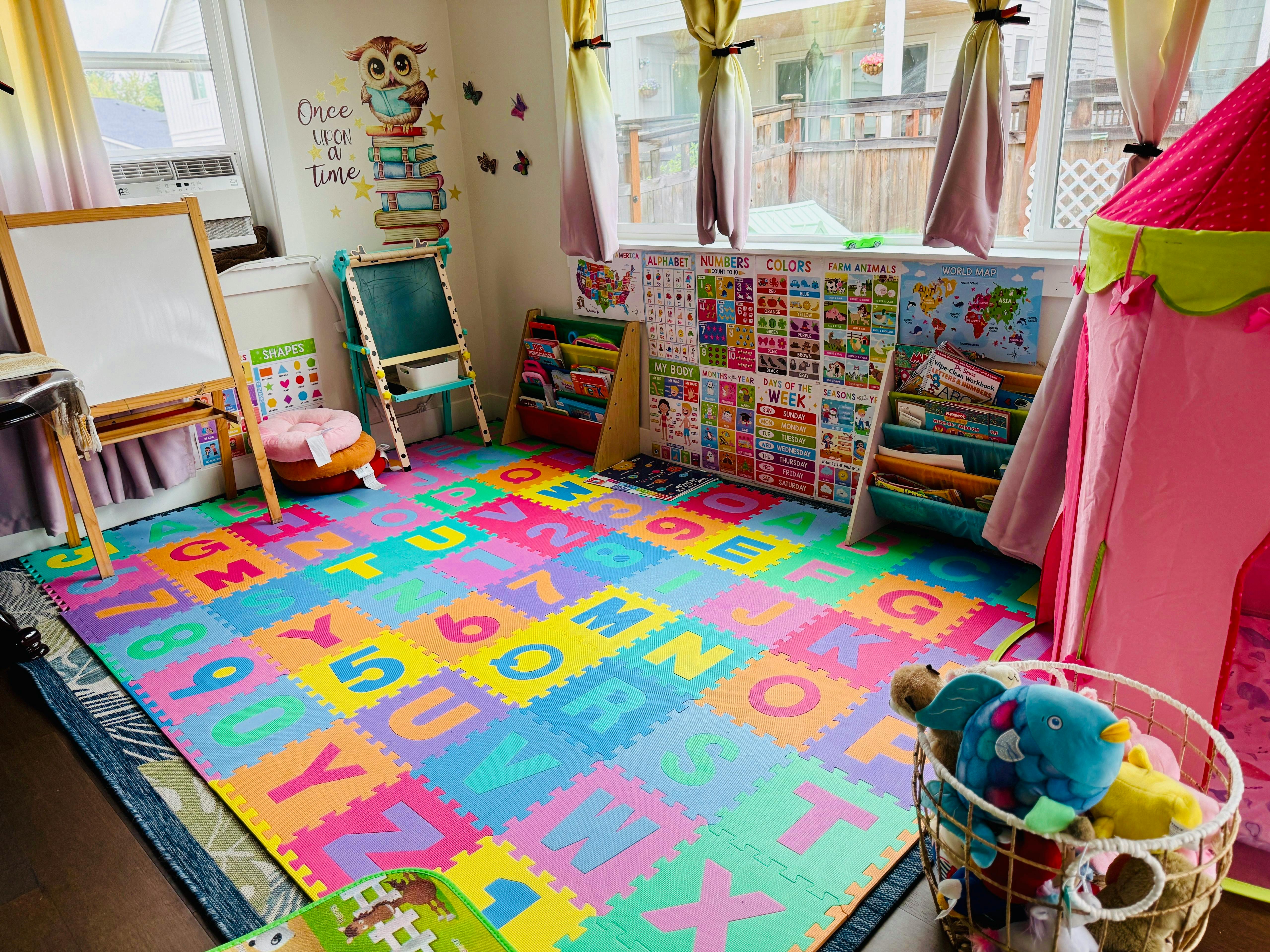 Playroom with colorful alphabet floor mats, easels, and a pink play tent