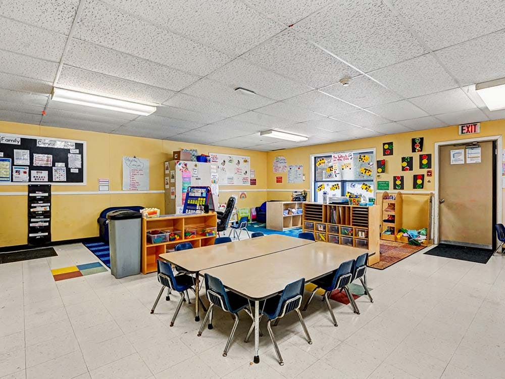 Empty colorful preschool classroom with tables, chairs, and learning materials