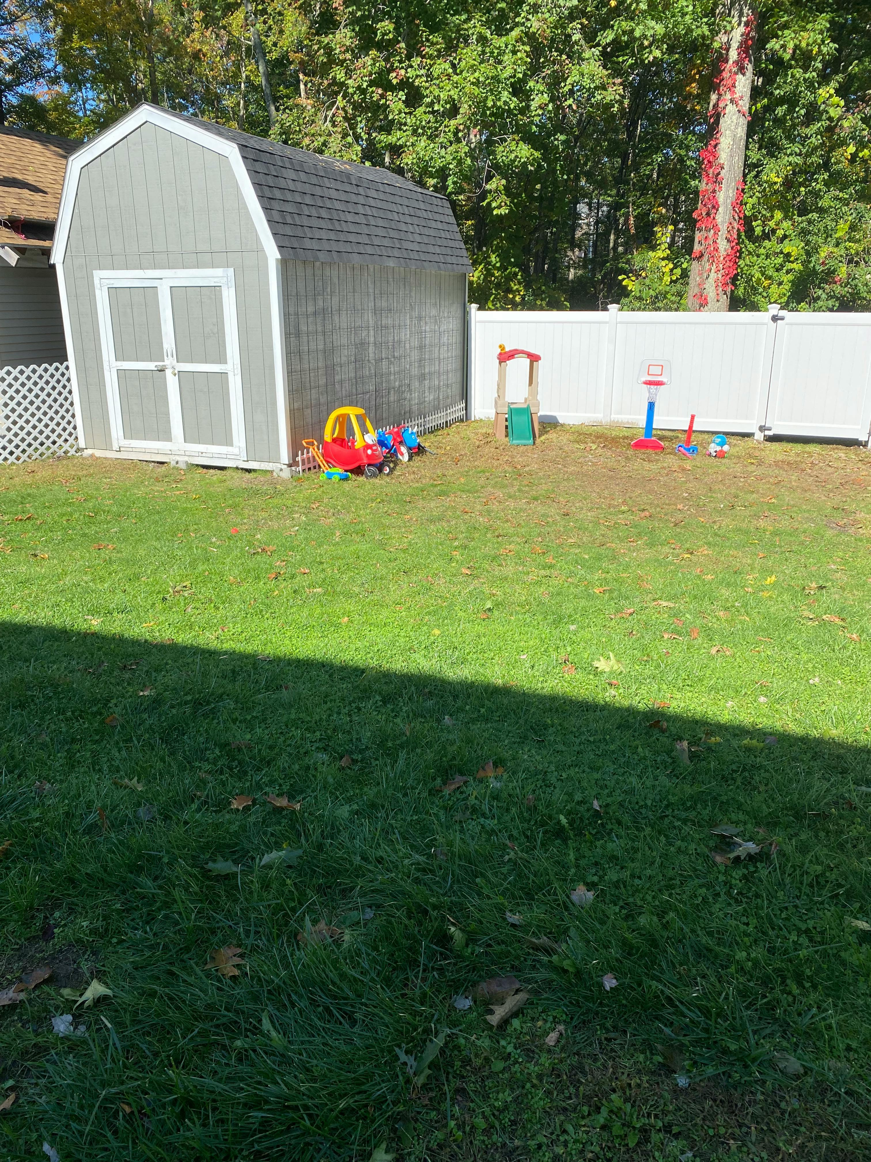 Gray shed with white trim in a backyard with toys and children's toys