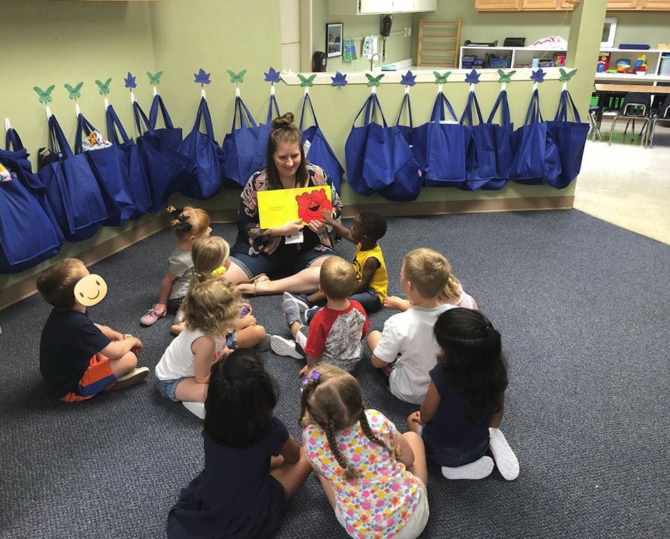 Person reading a book to a group of children sitting on the floor