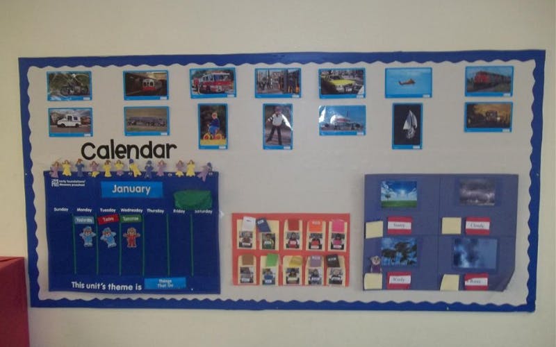 Classroom bulletin board with a calendar, photos of vehicles, and weather display