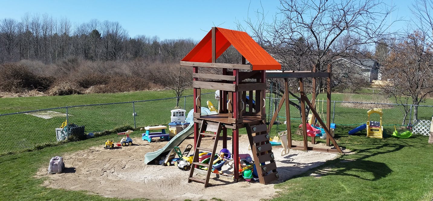 Outdoor playground with a wooden playset, slide, and swings