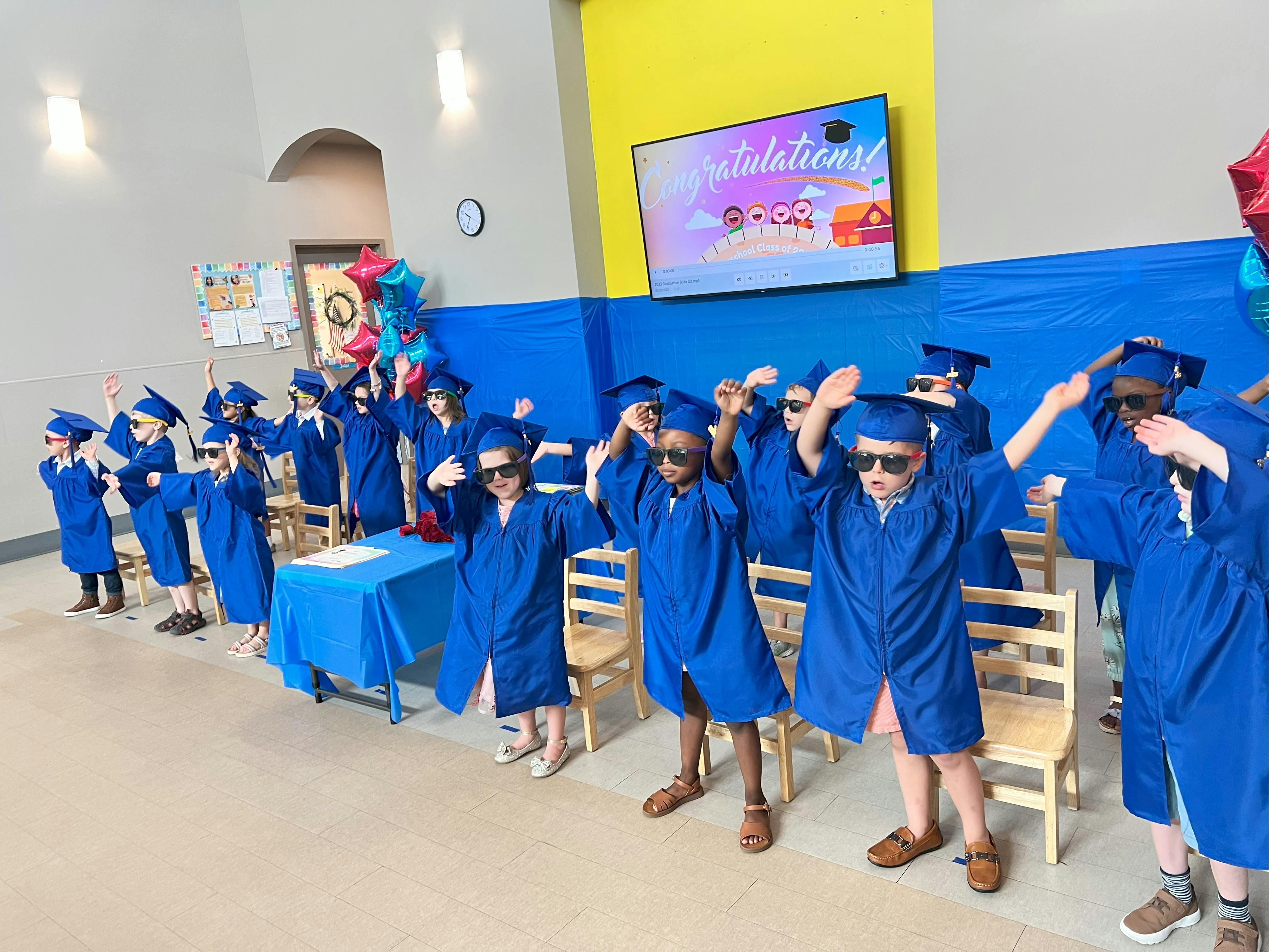 Children in blue graduation gowns and sunglasses raising their arms