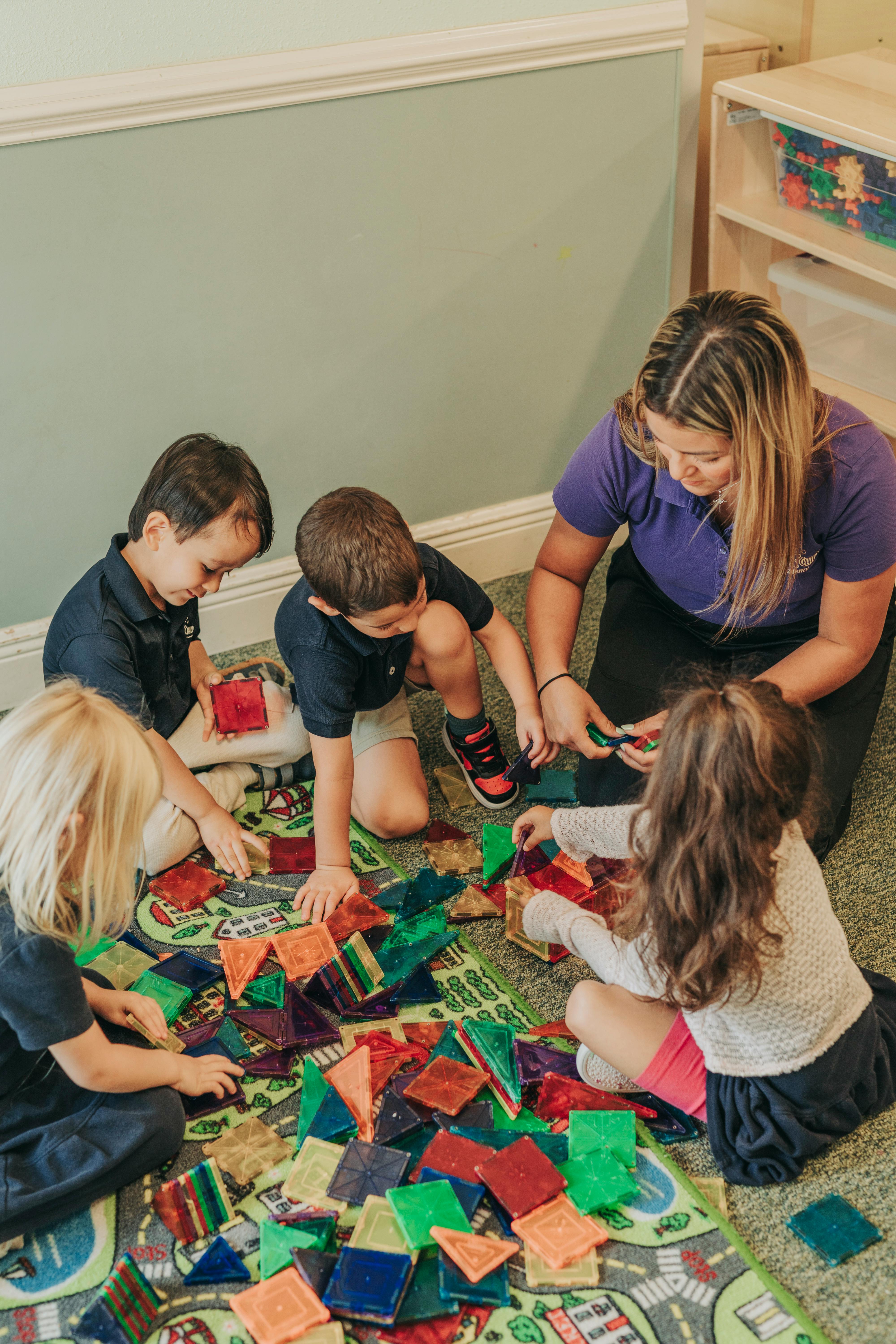 Adult and three children playing with colorful magnetic tiles on a rug