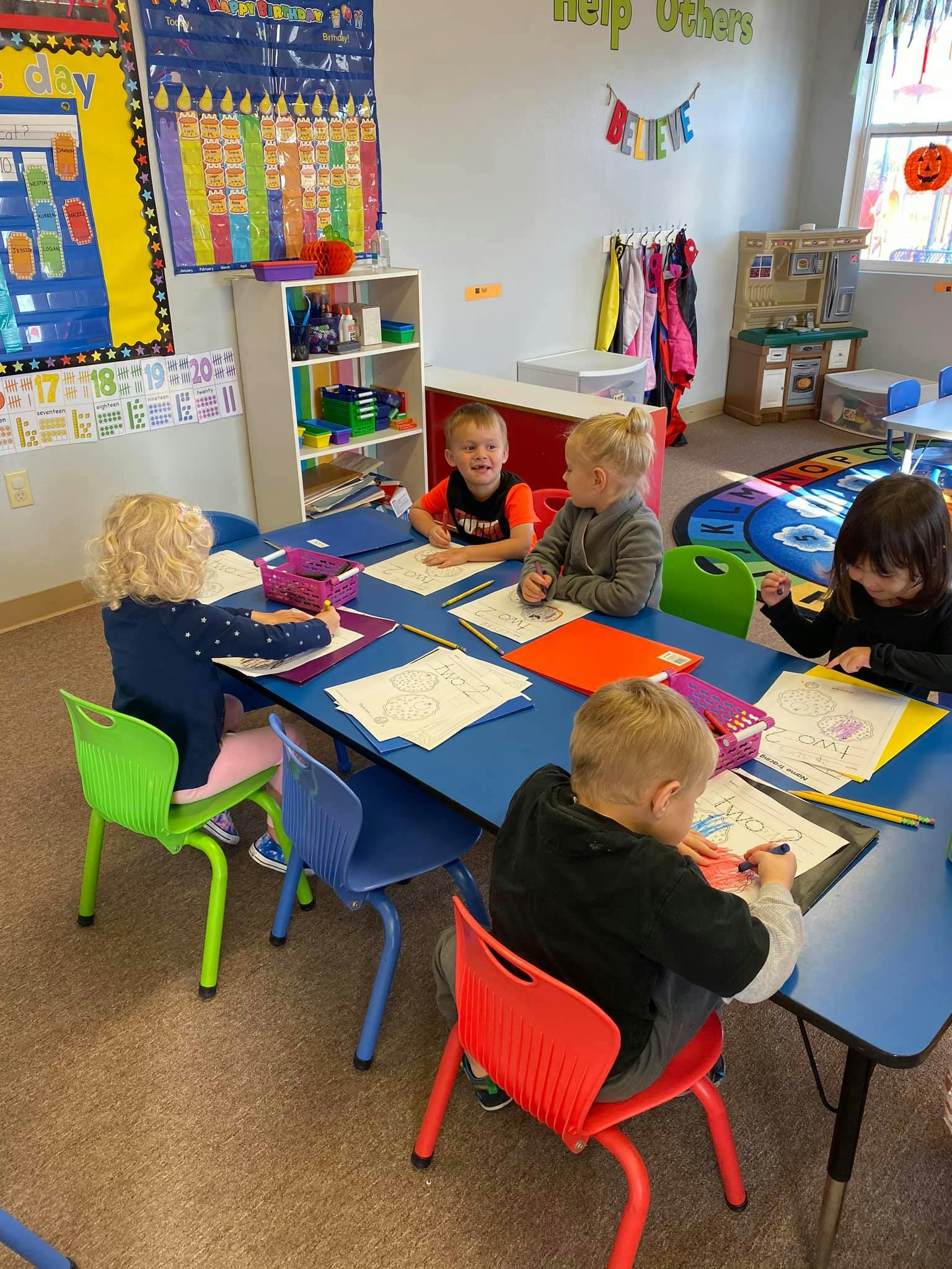 Children sitting at a table drawing and coloring in a classroom