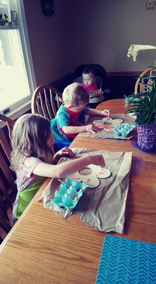 Three children painting flower cutouts at a table