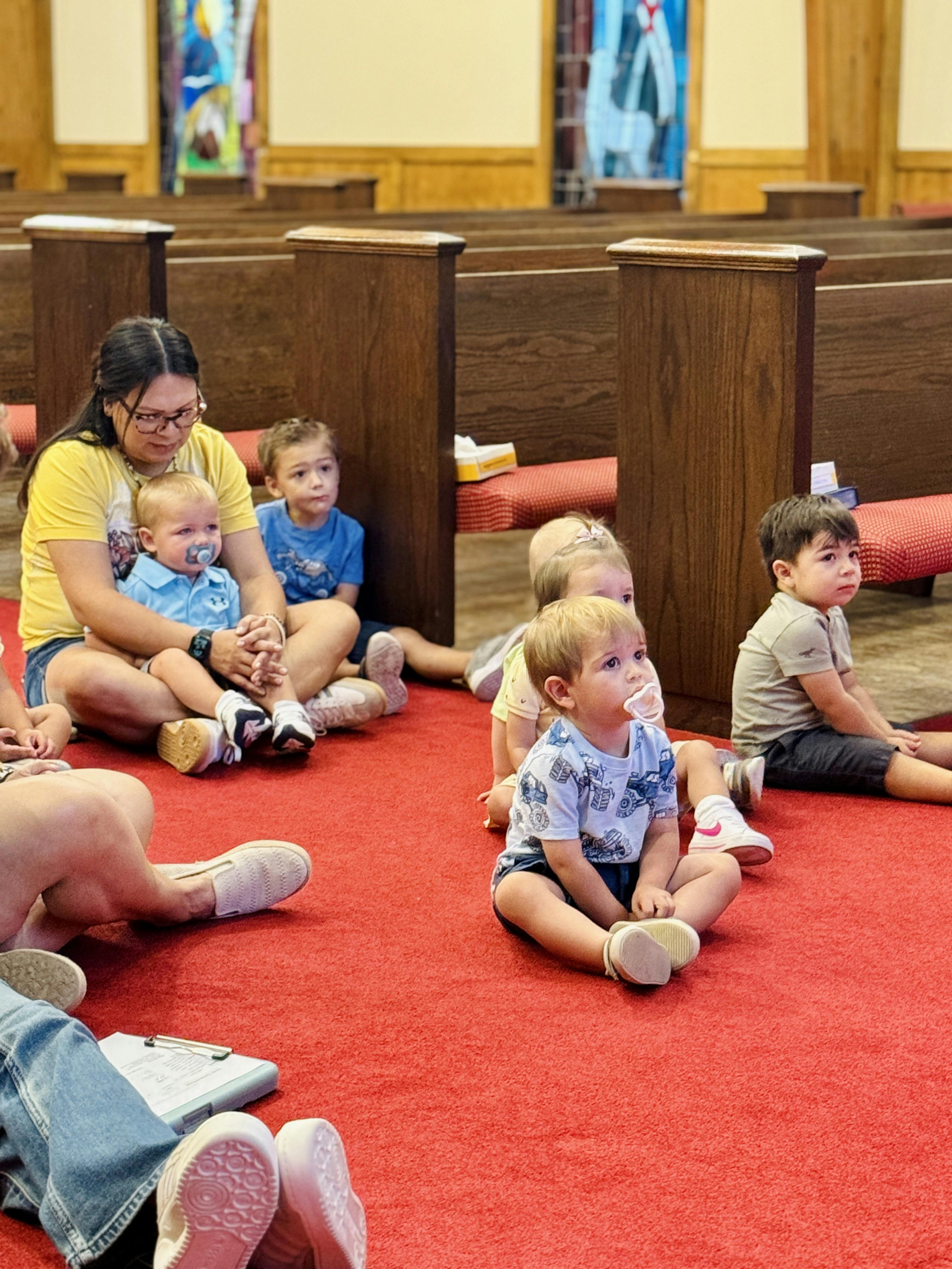 Adult and several young children sitting on a red carpet in an auditorium