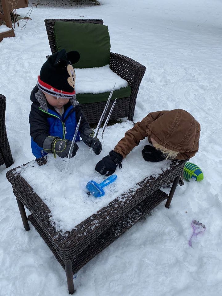 Two children playing in the snow around a patio table