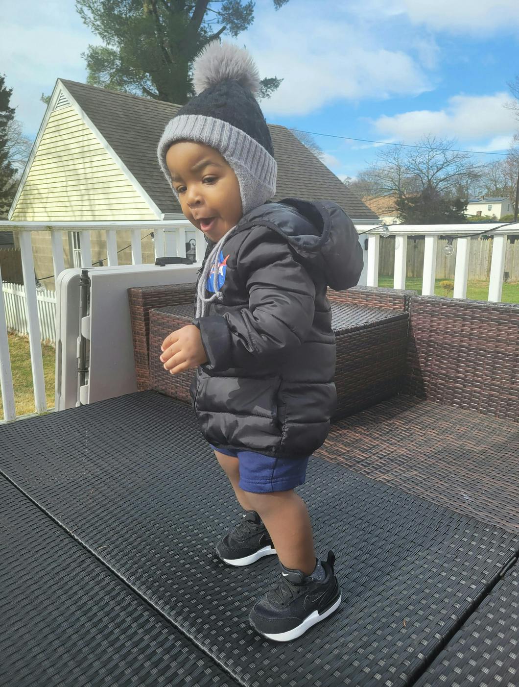 Child in a winter hat and jacket standing on an outdoor patio