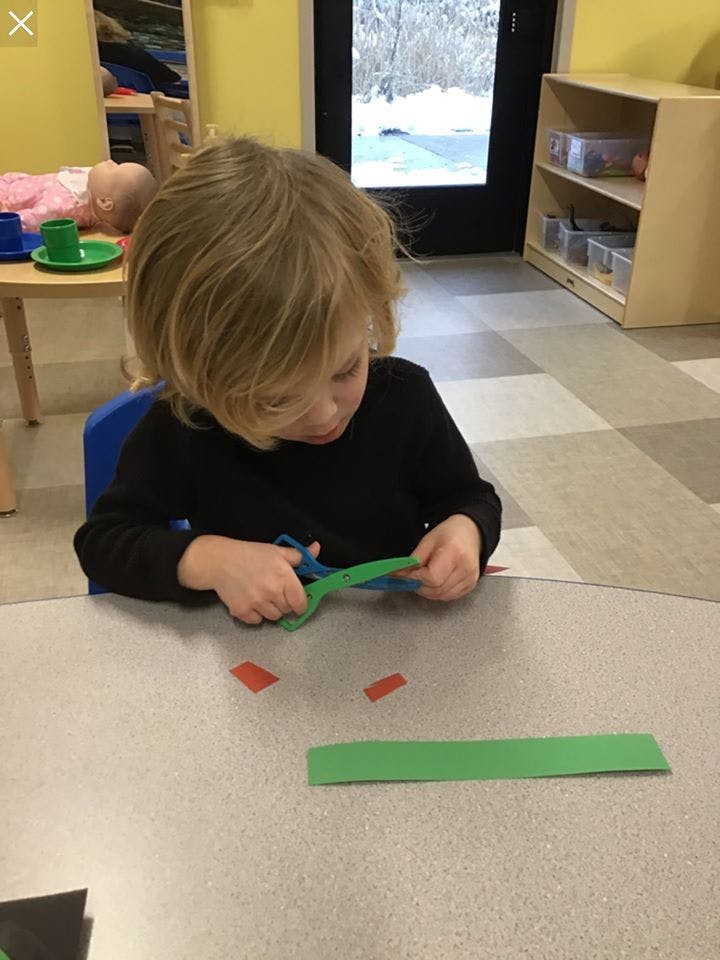 Child cutting green paper with scissors at a table