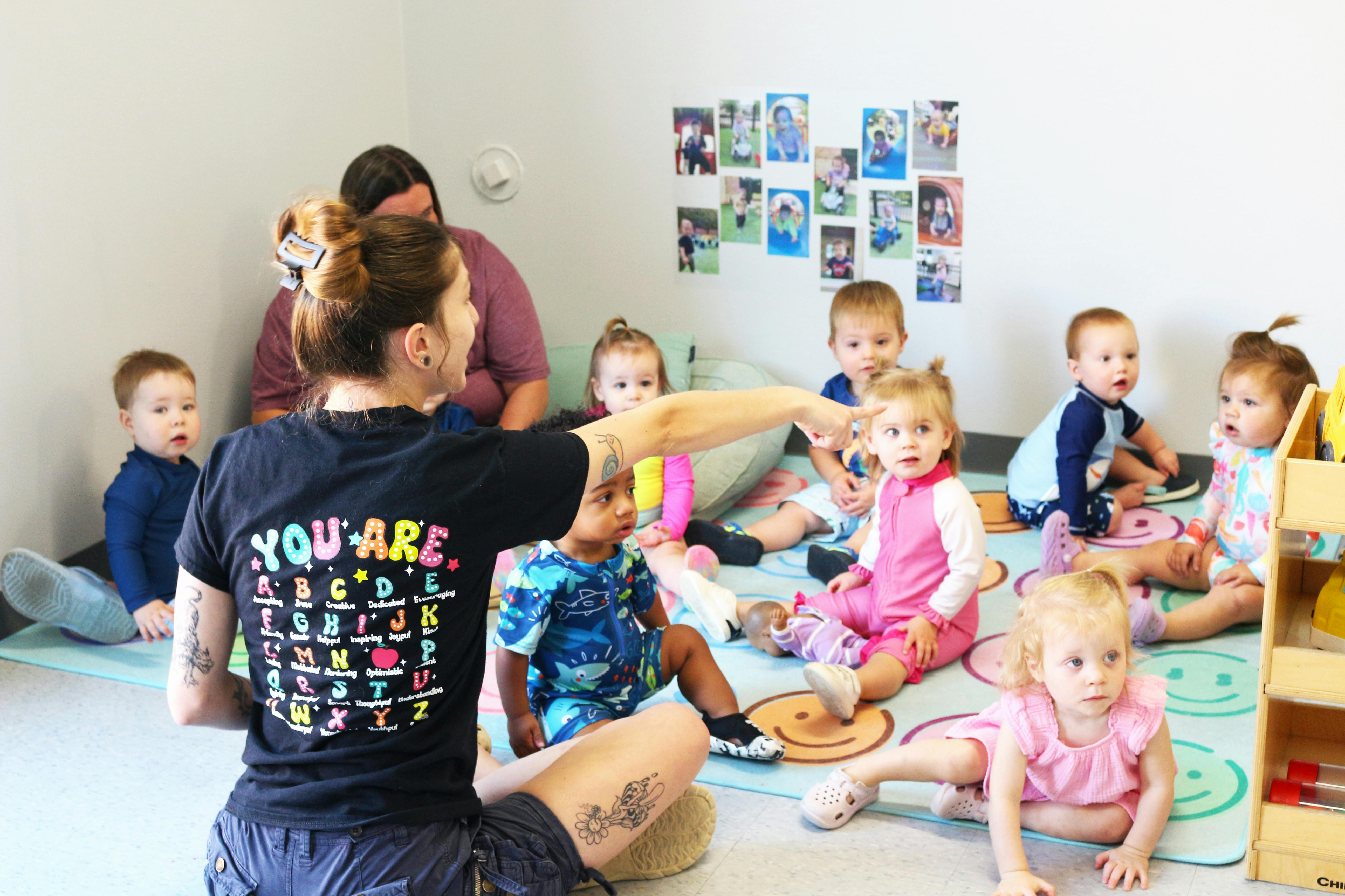 Person in black shirt pointing to a group of children sitting on the floor