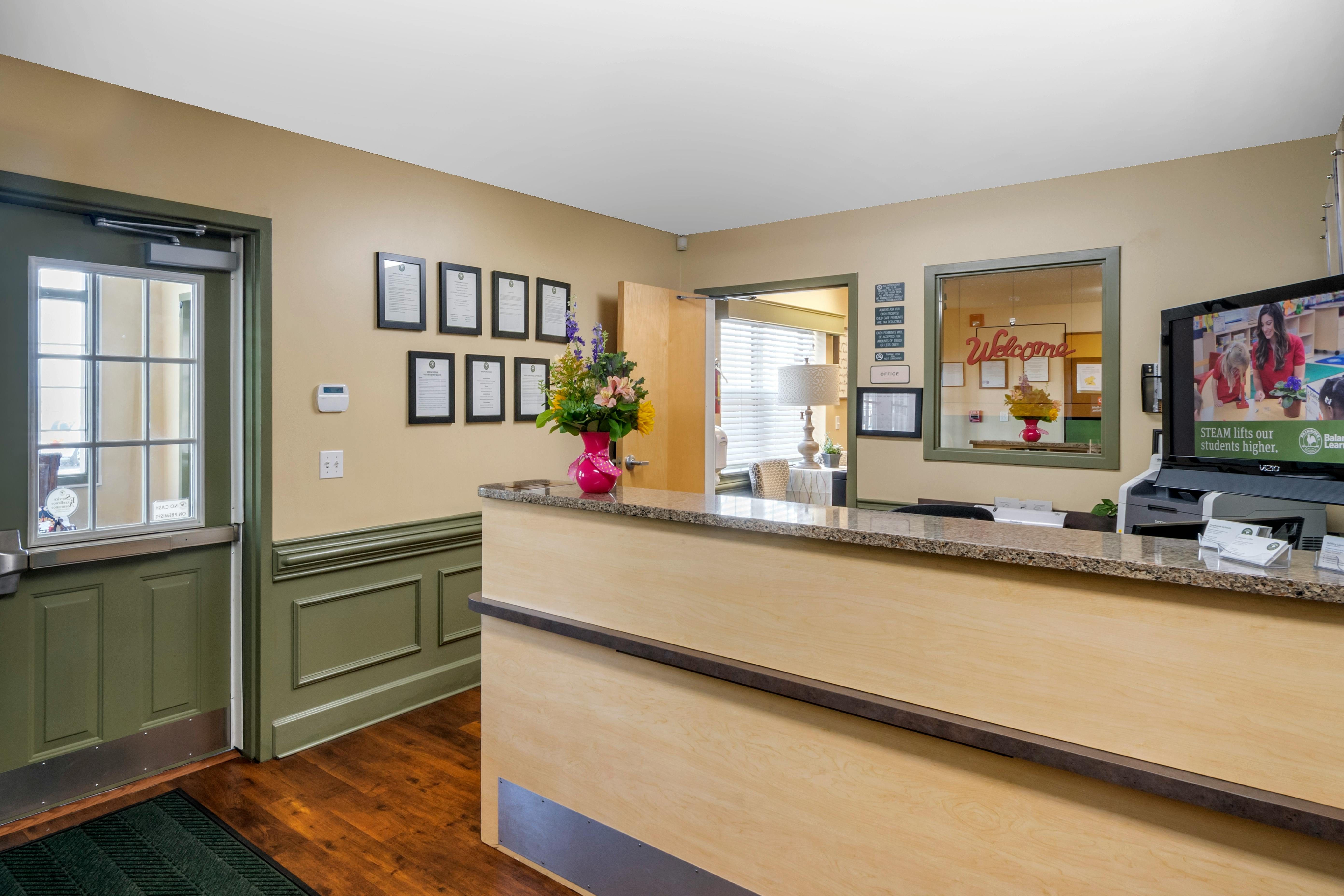 Reception area with a light wood counter, a TV, and a door on the left