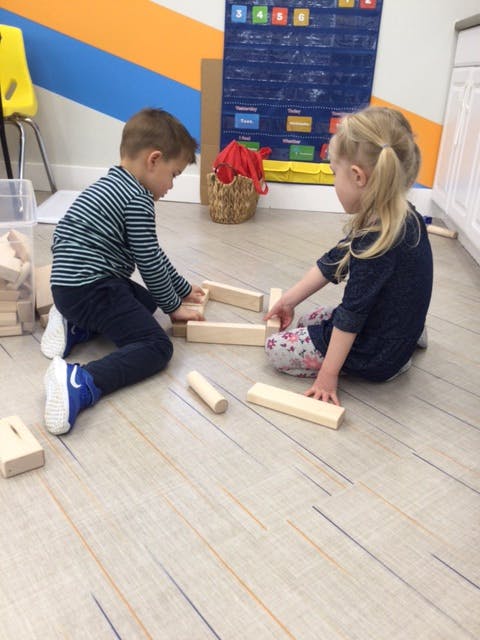 Two children playing with wooden blocks on the floor in a classroom