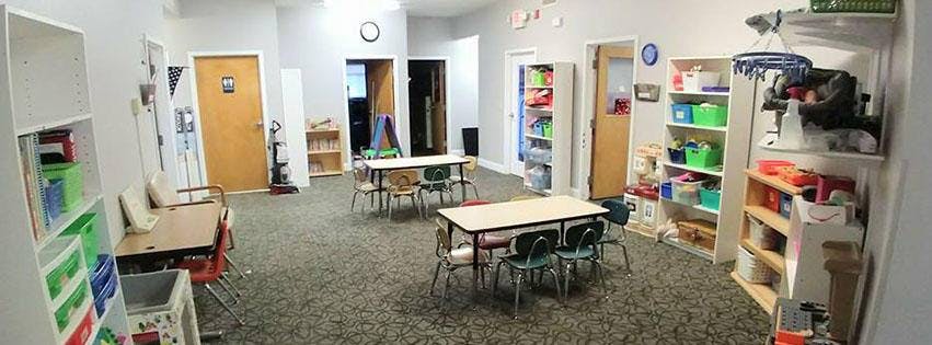 Classroom with small tables and chairs, shelves with supplies
